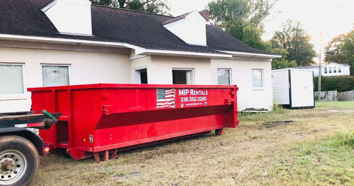 Bright red dumpster placed outside a residential building with MIP Rentals contact info displayed — ideal for Dumpster Rentals in Guilford & Rockingham.